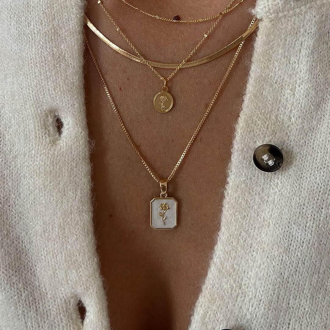 אדם הלובש סוודר סרוג בצבע שמנת עם שלוש שרשראות זהב בשכבות, כולל תליונים ותליון מלבני עם עיצוב מובלט.